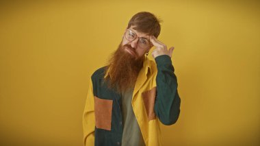 Sakallı düşünceli genç bir adam sarı arka planda poz veriyor, modaya uygun, düşünceli bir hava yayıyor..