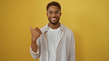 Yakışıklı bir adam, sarı bir arka plana başparmağıyla yan tarafı işaret ediyor.