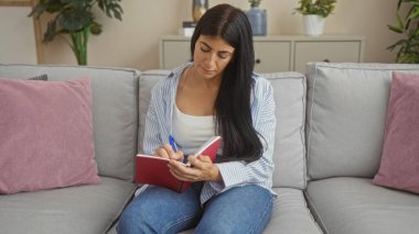 Güzel, genç bir İspanyol kadın, rahat oturma odasındaki kanepede otururken bir deftere yazıyor..