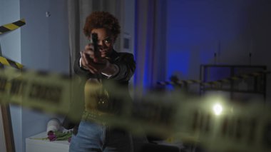 Focused african american woman aiming a gun indoors at a crime scene. clipart