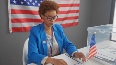 Mavi ceketli Afro-Amerikalı kadın Amerikan bayrağı taşıyan bir Amerikan üniversitesinde oy pusulalarını inceliyor..