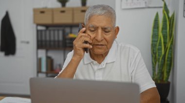 Ofiste oturan, dizüstü bilgisayarla konuşan, gri saçlı, yaşlı İspanyol bir adam..