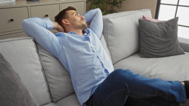 Modern bir oturma odasındaki kanepede dinlenen yakışıklı genç adam içeride huzurlu bir anın tadını çıkarıyor..