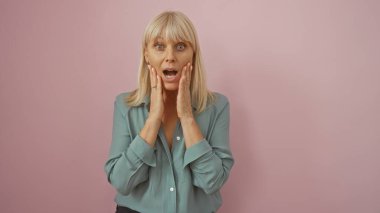 Mavi bluz giyen, soyutlanmış pembe arka planda elleri olan bir kadın şaşkınlığını ifade ediyor.