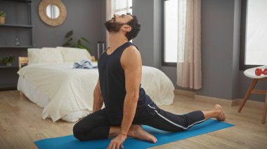 Adam yoga yapıyor, modern bir yatak odasında, sağlığını ve ev egzersizlerini yansıtıyor..
