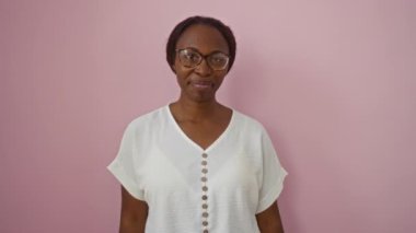 Dişleri olan, gözlüklü, beyaz dişlere ve izole edilmiş pembe arka planda sağlıklı ağızlara neşeyle bakan Afro-Amerikan bir kadın.