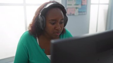 Parlak bir ofiste kulaklıkla çalışan bir kadın, profesyonel iç mekan ortamında genç bir Afrikalı Amerikalı kadın için kapalı bir çalışma ortamı yaratıyor.