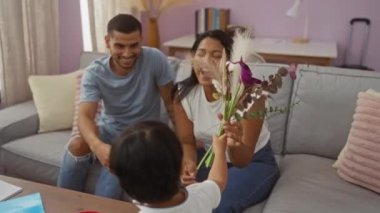 Oturma odasındaki çocuktan çiçek alan ve gülümseyen bir kadın ve erkek ile Latin bir aile.