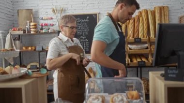 Kadın fırında ekmek ve hamur işleriyle erkeğin önlüğünü düzeltiyor.