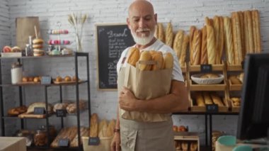 Fırında bir torba ekmek taşıyan gri saçlı adam çeşitli hamur işleri ve yiyeceklerle dolu.