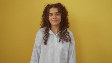 Tişört giyen genç İspanyol kadın mutlu bir şekilde gülümsüyor. Havalı bir gülümseme ve izole edilmiş sarı arka planda mükemmel dişlerle.