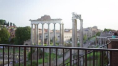 Odaklanamayan görüntü Roma harabelerini bulanık sütunlarla, açık bir gökyüzü altında tarihi mimari ve antik kültürü vurguluyor..