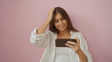 Pembe arka planda kumral saçlı genç bir kadın yüzünde endişeli bir ifadeyle akıllı telefonuna bakıyor.