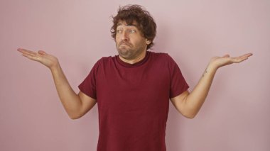 Şaşkın, sakallı, bordo gömlekli, pembe duvarda el kol hareketi yapan genç adam.