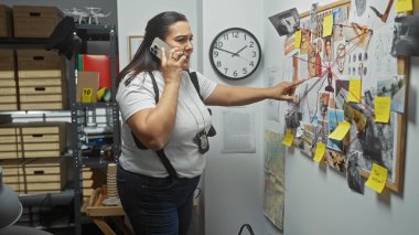 İspanyol kadın dedektif telefonda konuşurken bir karakolda kanıt panosunu inceliyor..