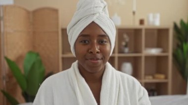 Güzel afro-amerikalı kadın sağlık spa odasında beyaz bir bornoz ve kafasında havlu ile öpücük yolluyor.