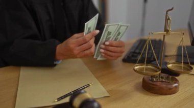 Yargıç masasında tokmak, denge ve bilgisayar olan bir ofis ortamında para sayıyor, profesyonel belgelerle dolu yasal bir ortamı vurguluyor..