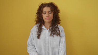 Genç İspanyol kadın izole edilmiş sarı arka plana karşı duruyor, gömlek giyiyor, kaşlarını çatıyor ve üzgün, bir soruna şüpheyle yaklaşıyor, olumsuz duygular gösteriyor.