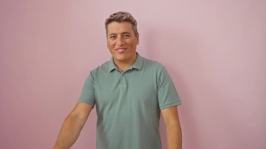 Zafer işaretiyle duran beyaz bir adam, göz kırpan bir surat, iki kişilik V, izole edilmiş pembe arka planda mutlu bir gülümseme.