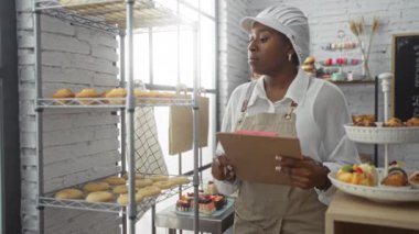 Pastanedeki genç Afrikalı Amerikalı kadın yanında hamur işleri raflarıyla envanterini kontrol ediyor.