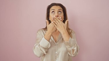 Şaşırmış İspanyol bir kadın, elleri ağzının üzerinde pembe bir arka plana karşı, zarafet ve duygu yayıyor..