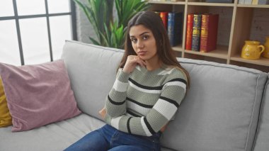 Düşünceli, genç bir İspanyol kadın şık bir oturma odasındaki kanepeye uzanmış, sıradan bir güzellik ve düşünceli bir zarafet sergiliyor..