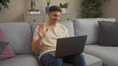 Yakışıklı bir İspanyol, samimi bir oturma odasında dizüstü bilgisayarla sohbet ederken el sallıyor..