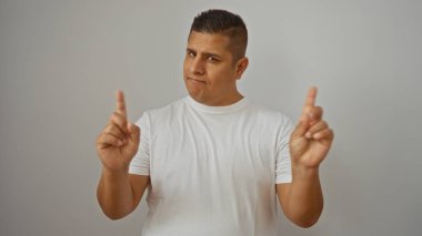 Genç İspanyol adam, beyaz bir arka plan üzerine beyaz gömlek giyerek onaylamayan bir jest yapıyor.