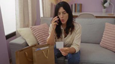 Oturma odasında alışveriş yaparken telefonla konuşan genç bir kadın. Yanında alışveriş torbaları var.
