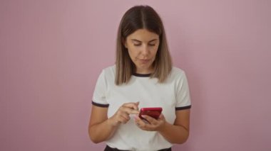 Genç bir kadın pembe arka planda gülümserken akıllı telefon kullanıyor.