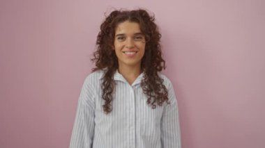 Pembe arka planda soyutlanmış genç bir kadın gülümsüyor ve çizgili bir gömlek giyerken öpücük yolluyor.