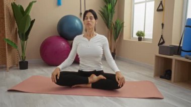 Egzersiz malzemeleri ve bitkilerle çevrili yoga minderiyle meditasyon yapan bir kadın.
