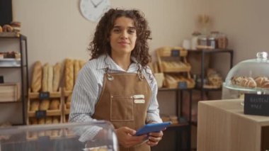 Fırın odasında elinde tablet olan genç bir kadın. Arka planda da ekmek rafları var.