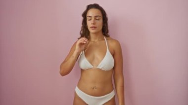 Bikinili genç bir İspanyol kadın. Kulaktan kulağa dedikodu dinliyor. Pembe arka planda izole edilmiş.