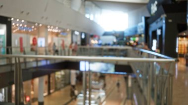 Dışlanmış insanların yürüdüğü ve arka planda parlayan ışıkların olduğu bir alışveriş merkezinin içi bulanık.