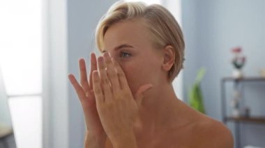 Genç, sarışın, sağlık merkezinde bir kadın, kaplıca odasında nazikçe yüzüne dokunuyor, güzellik ve rahatlama ruhunu yakalıyor.