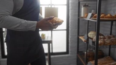 Sakallı ve kel kafalı Afrikalı Amerikalı bir adam sıcak bir fırının içinde ekmek ve hamur işleri düzenliyor..