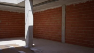 Bokeh arka planında kısmen inşa edilmiş çatının altında kırmızı tuğla duvarlar ve gri beton sütunlarla tamamlanmamış bir inşaat alanının bulanık görüntüsü