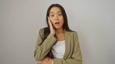 Beyaz bir arka plan duvarında izole edilmiş bej ceketli güzel Çinli kadın şaşırmış görünüyor.