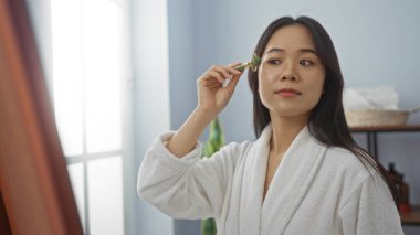 Kaplıcadaki Asyalı kadın cilt bakımı için yeşim taşıyla dolaşırken saglik odasında yumuşak, hafif bir beyaz bornoz giyiyor..