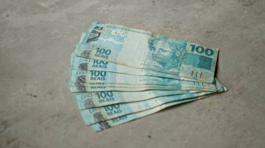 Brezilya 'nın gerçek para birimini gösteren beton bir yüzeye yayılmış birkaç yüz Brezilyalı gerçek banknot..