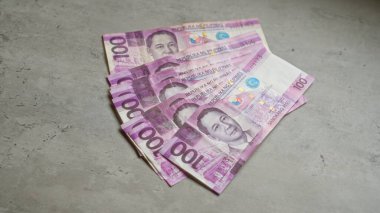 100 pesoluk banknotun sergilendiği beton bir yüzey üzerindeki Filipin banknotları.