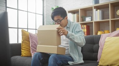 Asyalı bir adam ilginç bir şekilde modern bir oturma odasında karton bir kutuyu açıyor..