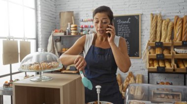 Lezzetli ekmek ve hamur işleriyle dolu bir fırında çalışan bir kadın telefonda konuşuyor.