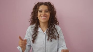 Genç bir kadın pembe bir arka plana neşeyle gülüyor, güzel esmer buklelerini ve canlı kişiliğini sergiliyor.