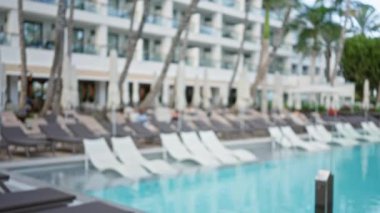 Lüks havuzu bulanık manzaralı tropik bir tatil yeri ve palmiye ağaçlarının altında şezlonglar.