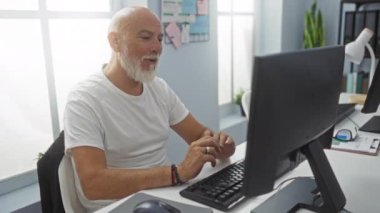 Ofis odasında çalışan, yüzünde bir gülümsemeyle klavyede yazan olgun bir adam.