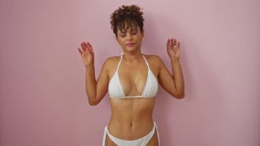 Bikinili, uykulu, genç, İspanyol bir kadın. Ağzının üstünde duruyor. Pembe, soyutlanmış arka plana karşı yorgun ve sıkılmış.