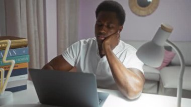 Evde dizüstü bilgisayarla çalışırken, etrafı kitaplarla çevrili ve beyaz bir masa lambasıyla aydınlatılmış yorgun genç adam esneme hareketleri yapıyor..