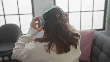 Bir kadın rahat bir oturma odasında kulaklıklarını ayarlıyor, rahatlama ya da rahatlama öneriyor..